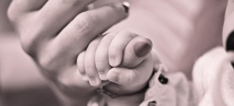 Baby holding mother's finger depicting secure attachment.